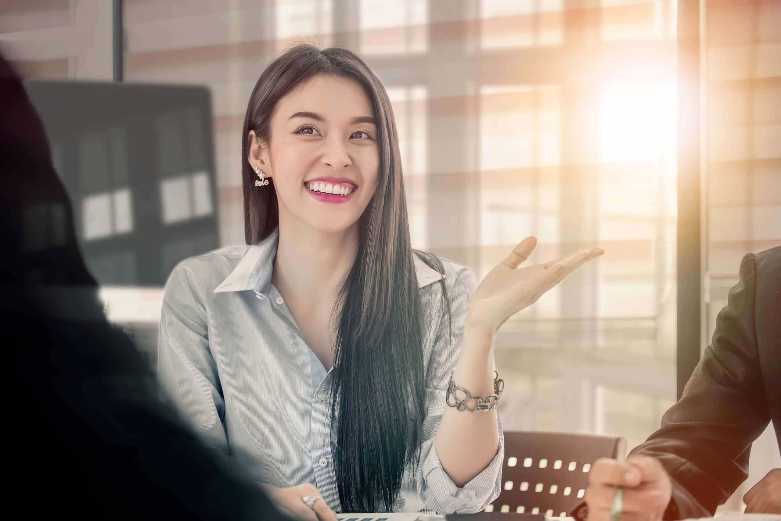 Woman sitting at office table, smiling with sunlight coming in.